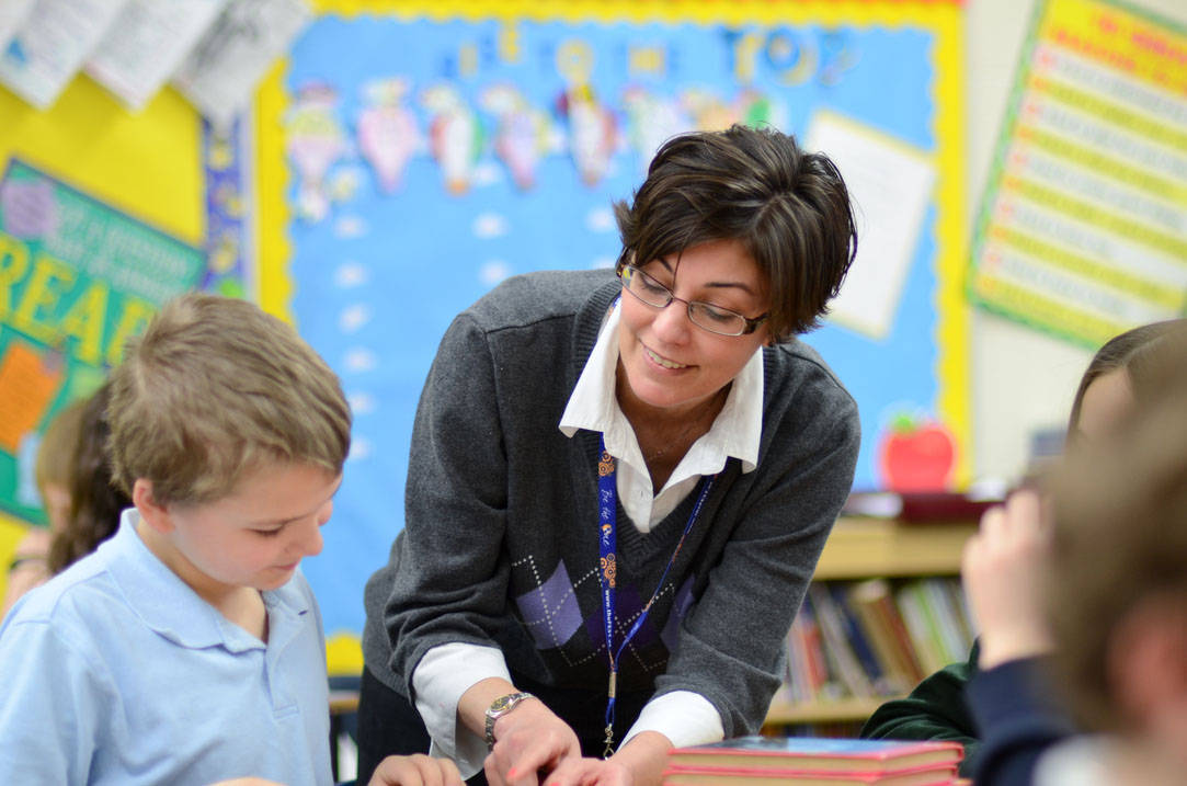 Teacher helps young student with reading assignment